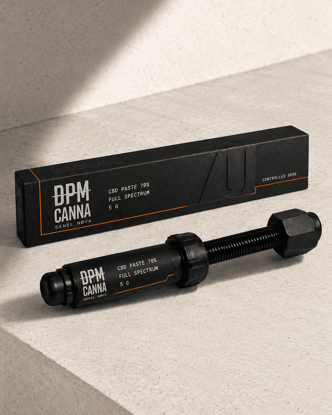A black CBD paste syringe in front of its box on pale stone